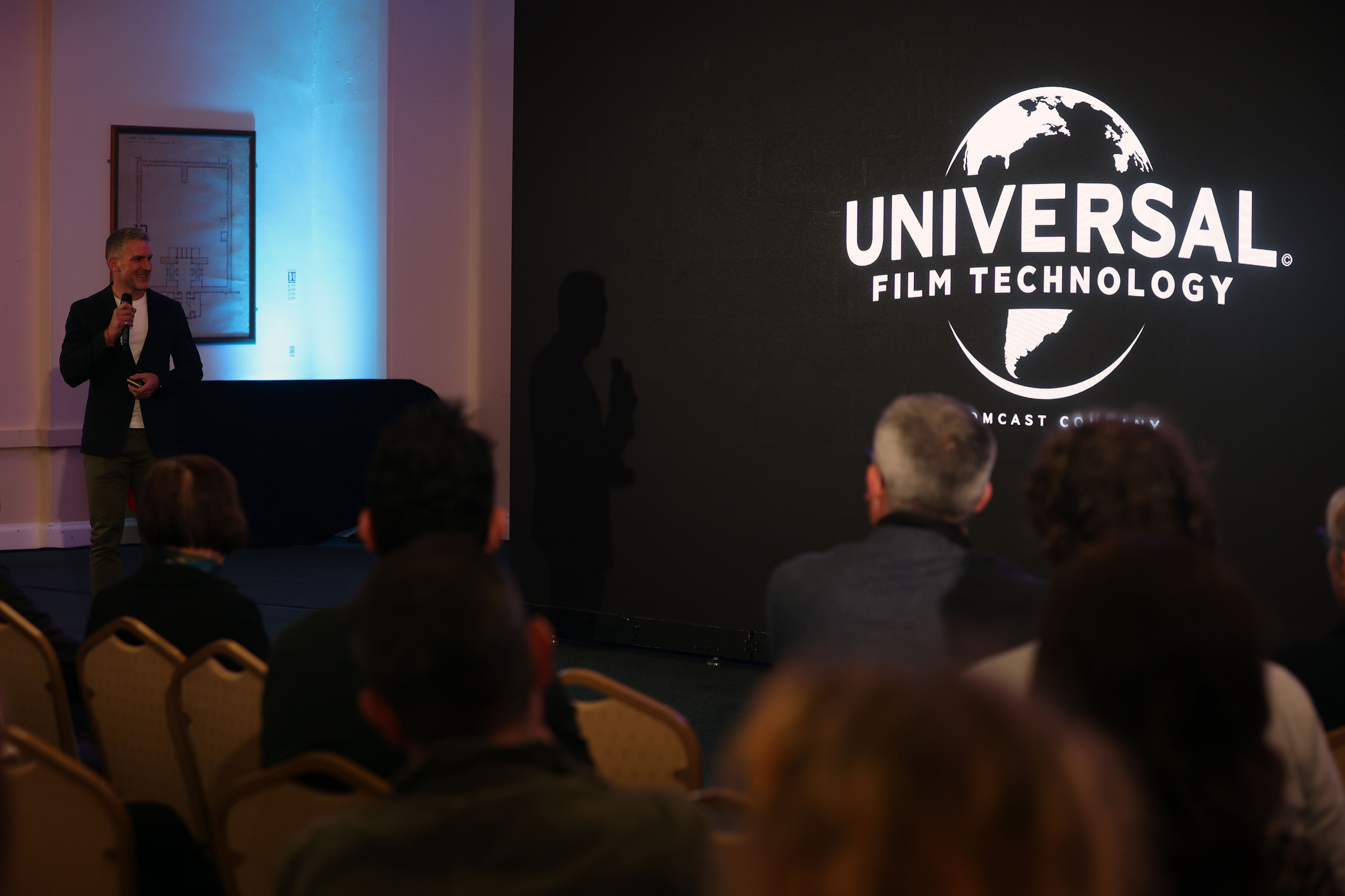 Greg Reed presents at ClwstwrVerse infront of LED screen featuring Universal Pictures logo