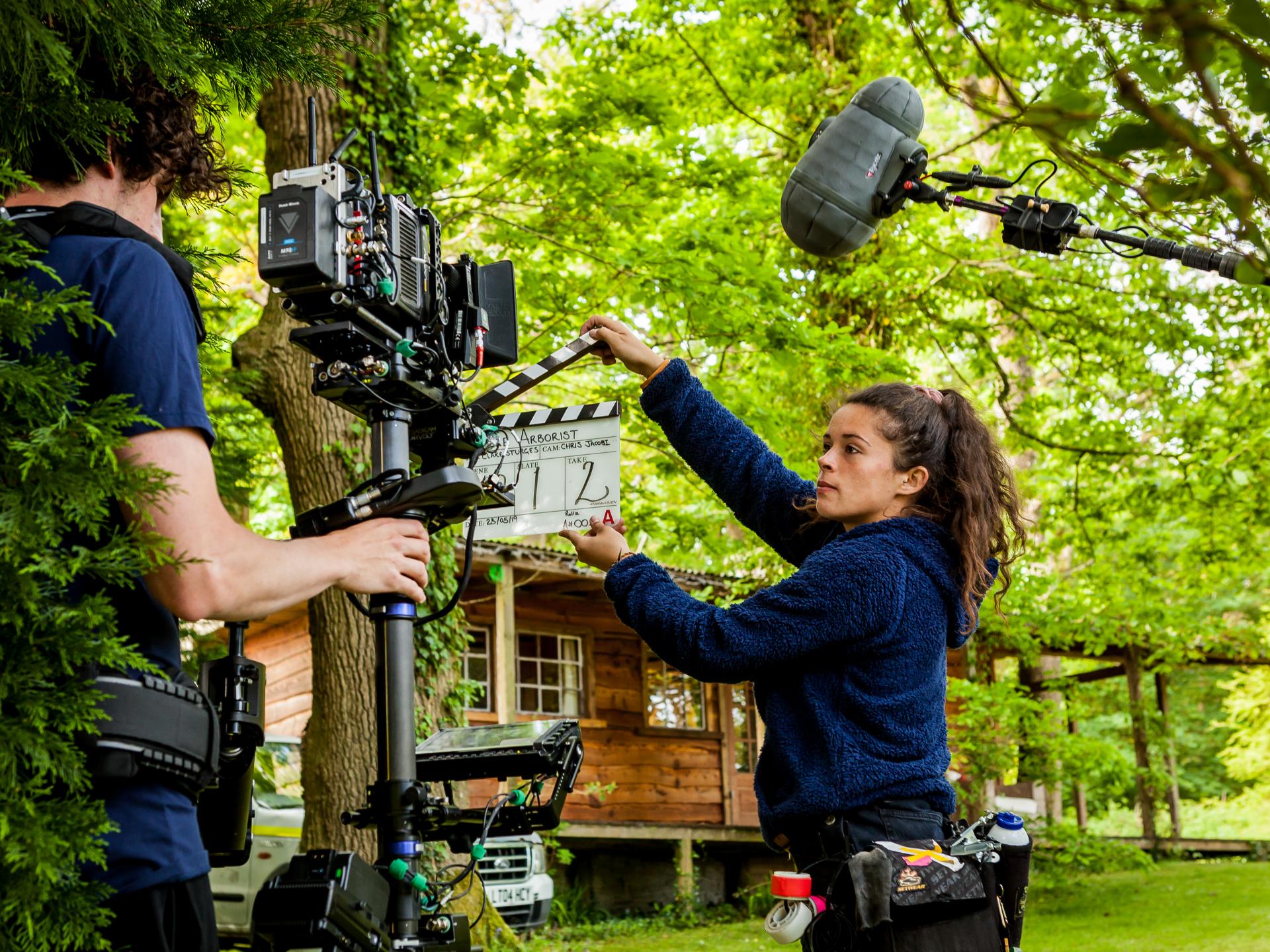 Man holding a camera and women holding a clapperboard in the forest. Credit: Arborist - Tom Sparey